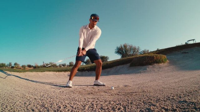 A golfer hits perfect shot out of fairway bunker, spraying sand toward the green under a clear sky in slow motion, 4k 800fps wide angle tracking shot