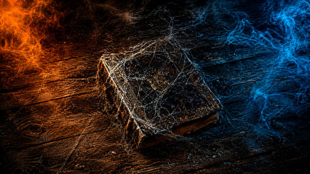 Ancient spellbook covered in spiderwebs on a rustic wooden table. Dark magic grimoire with orange fire and blue smoke effects. Spooky Halloween fantasy background