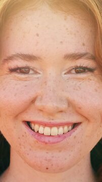 Close up portrait of a beautiful young woman with red hair and many freckles. Smiling happily and looking at the camera. Showcasing her natural beauty and positive emotion in a sunny outdoor setting