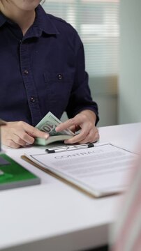 Realtor counting a stack of hundred-dollar bills at the office desk. A client is making a cash payment for a property after signing the contract.