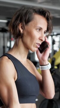 Athletic businesswoman multitasking in the gym, talking on her mobile phone with a business partner while performing bicep curls with a dumbbell, showcasing work life balance and dedication