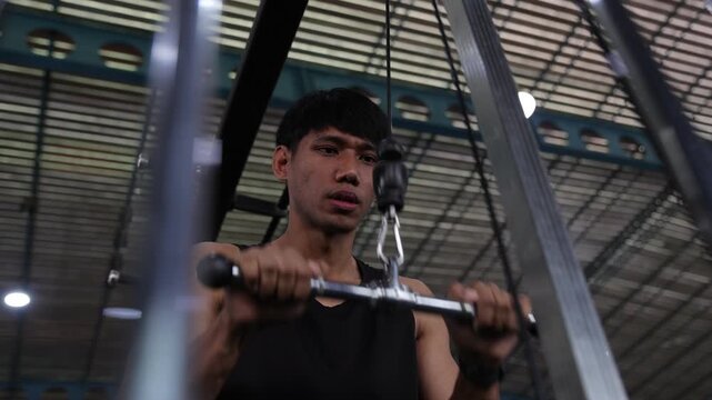 Determined Asian man doing triceps pushdown workout at the gym.