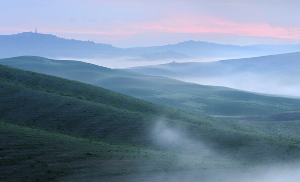 Morning atmosphere in Tuscany, hilly landscape with fog at dawn, behind the city of Pienza, Val d'Orcia, Tuscany, Italy