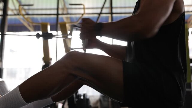 Muscular Asian man doing seated cable row exercise in the gym.