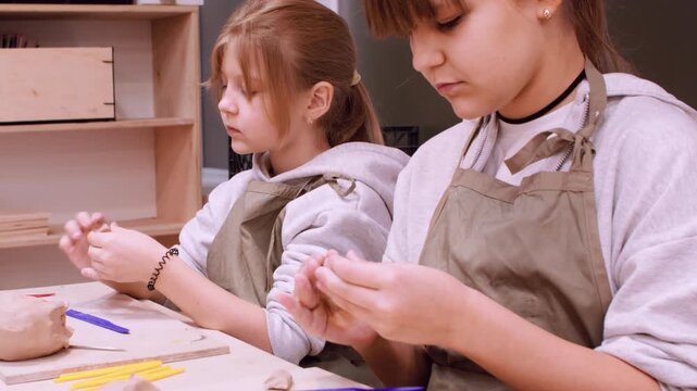 Talented craft. Creative learning. Two inspired children shaping ceramic molding raw clay using tool in professional master workplace.