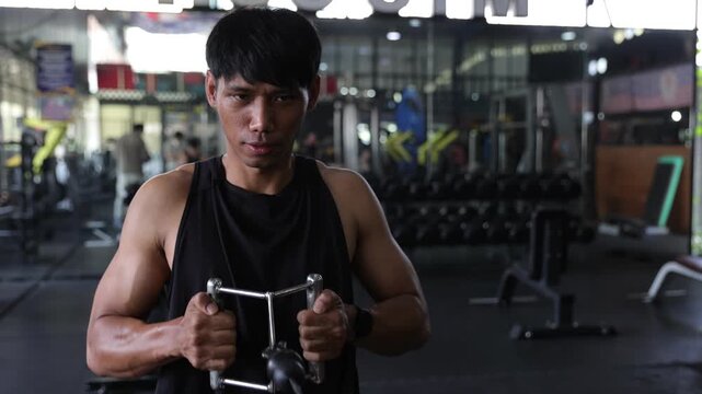 Young athletic Asian man training his back and biceps muscles using a seated cable row machine. Intense workout session for strength and endurance.