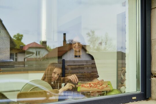 View through the window of a mother and daughter preparing a salad in the kitchen
