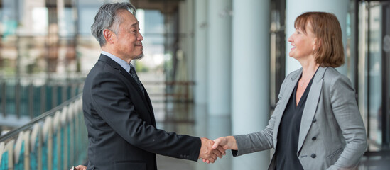 Two diverse senior business professionals shaking hands for greeting after successful deal discussion in modern office environment representing partnership agreement and corporate collaboration. © BESTIMAGE