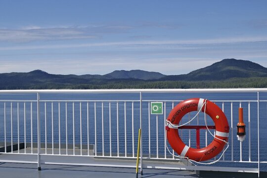 View of the sea from a ship with a lifebuoy and mountains in the background under a clear sky, BC Ferries ferry in the Inside Passage on the route to Prince Rupert