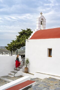 Young woman with red skirt at a Cycladic white and red Orthodox church, Paleokastro Monastery, Mykonos, Cyclades, Greece