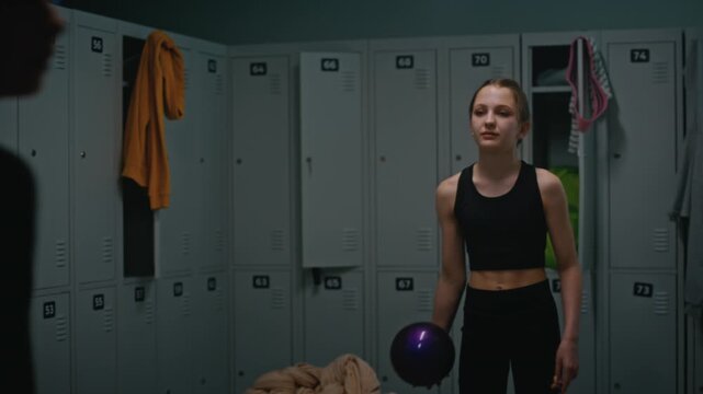 Young Female Athletes Practicing With Purple Rhythmic Gymnastics Ball in Changing Room. One Focused Girl Catches The Ball, Teammate Throws It. Entertainment For Teenagers Waiting For Gymnastics Class.