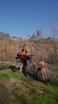 Portrait of smiling caucasian artist plays wooden acoustic guitar in autumnal park. Young songwriter plays string musical instrument hobby outside in nature fall time. Audio music healing in natural