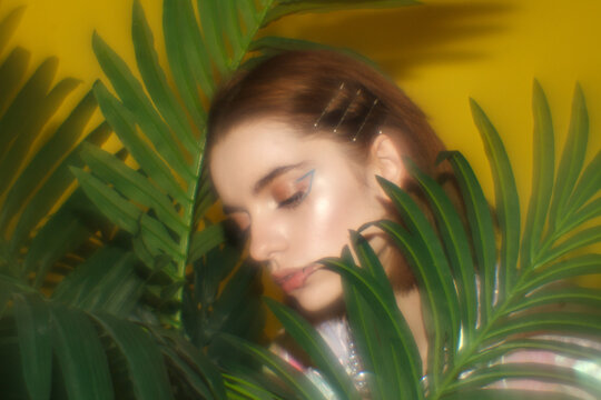 Soft portrait of a young woman surrounded by tropical leaves on a vibrant yellow background. Beauty, nature and skincare concept.