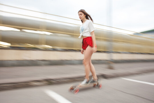 Young woman riding a longboard with motion blur in an urban environment. Speed, movement and active city lifestyle concept.
