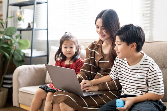 Happy Asian mother with children looking at laptop screen together on sofa at home