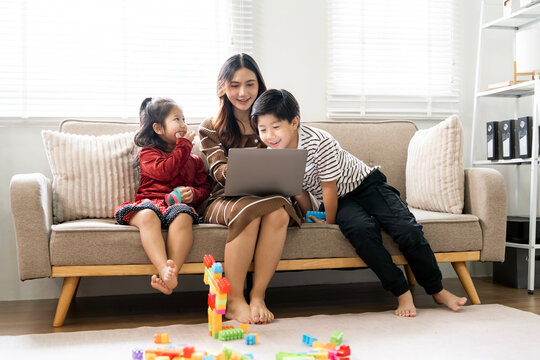 Asian mother and children using laptop together on sofa in living room at home