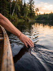 Fototapeta premium Hand Trailing Through Clear Water From Side of Wooden Canoe at Sunset
