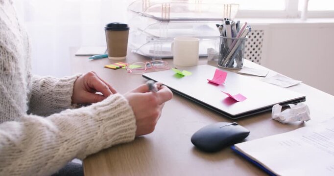 Work lifestyle. Business paperwork. Unrecognizable female manager at desk writing using sticky notes on laptop in office indoor.
