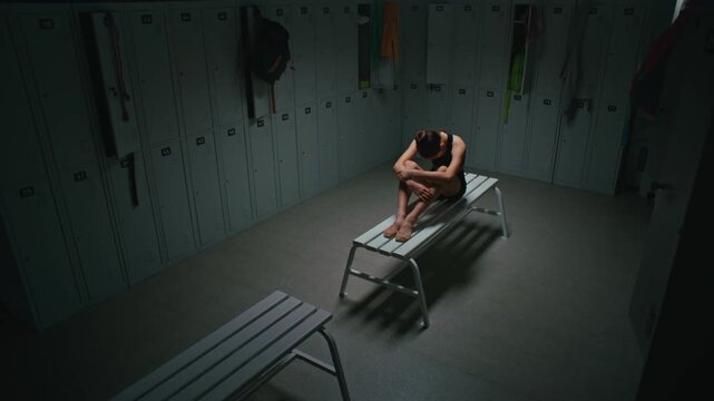 Depressed or Exhausted Teenage Athlete Sitting Alone on Bench, Hugging Knees With Arms. Girl Experiences Moment of Psychological Burnout, Pressure, Failure, or Deep Fatigue After Hard Workout.