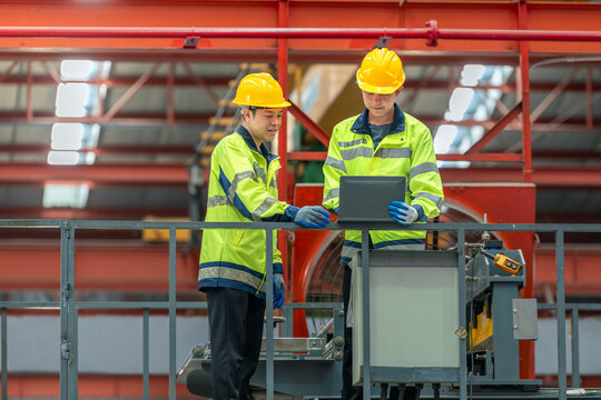 Engineers team inspecting metal sheet machine system inspection check collaboration in factory Two male engineer partner wearing safety uniform with helmet looking monitors machinery operation