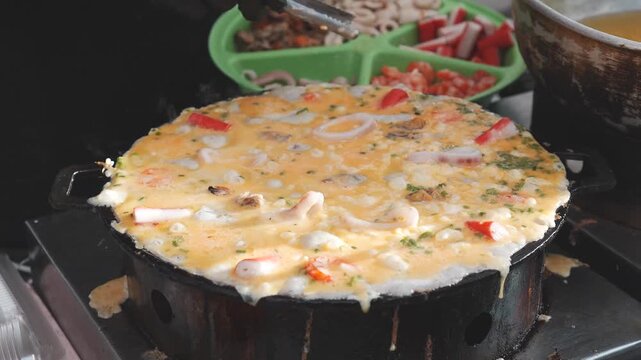 Seafood pieces added to sizzling egg dish on Thai street griddle