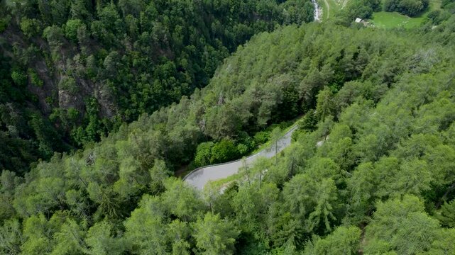 Drone follows a motorcycle riding along the scenic mountain road beside the Gorges du Durnand in Valais, Switzerland, surrounded by lush forests, cliffs and alpine landscapes.