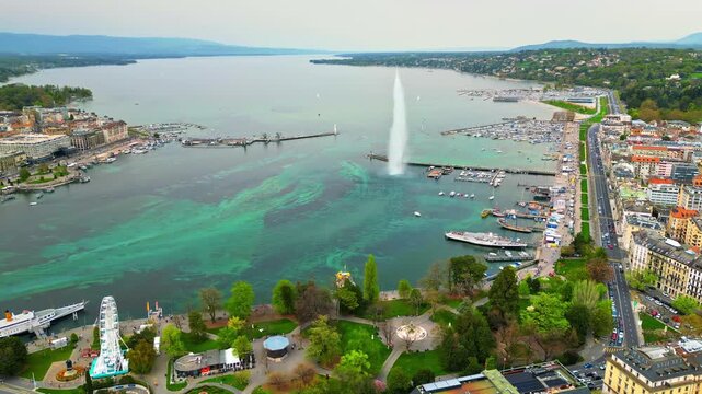 Aerial view of Geneva city and lake with Jet dEau fountain in motion, boats docked along port.