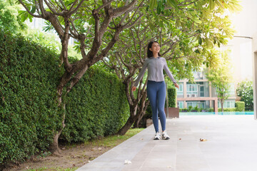 Fototapeta premium Asian Gen Z woman stretching body and twisting after workout in green urban park for wellness healthy lifestyle and fitness.