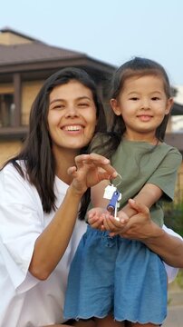 Joyful single mother and her adorable little daughter proudly showing the keys to their new home, celebrating a fresh start and the dream of homeownership becoming a reality