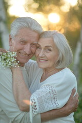 Fototapeta premium senior embracing outdoors at sunset with warm affectionate mood and flowers in the foreground close-up view on wooden surface background. white and green colors.