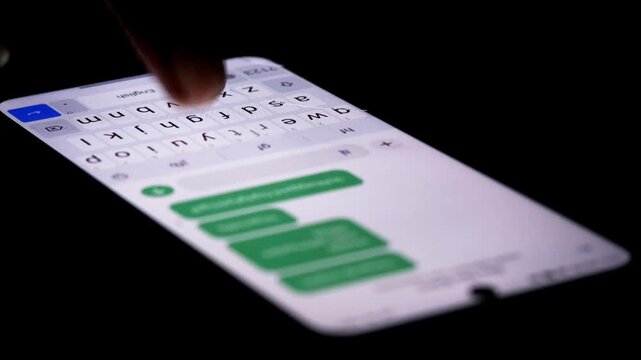 Night, hands typing repeated messages on a smartphone for spam messaging, anonymous communication, internet trolling, cyberbullying, and online harassment.