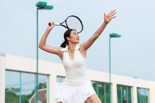 Asian young sportswoman exercise, playing tennis on outdoor clay court.