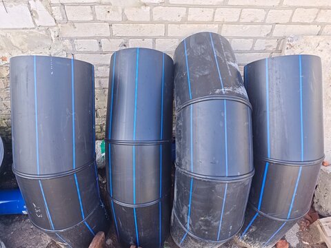 Black plastic HDPE pipes with blue stripe near a brick wall.