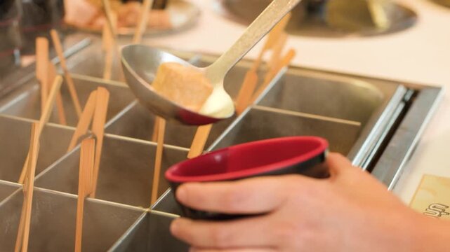 Ladle Pouring Hot Broth and Fish Cake into a Red Bowl