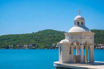 Obraz premium White stone baptistry Suza Njegoseva Tivat Montenegro by blue sea with green hills background, serene coastal landmark view.
