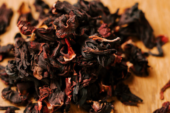 Dried red hibiscus flower petals resting on a light wooden surface during the bright afternoon light
