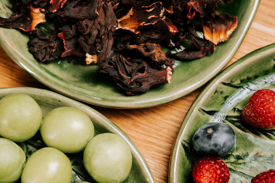 Dried Hibiscus flowers along with fresh grapes and berries on green plates for a healthy snack