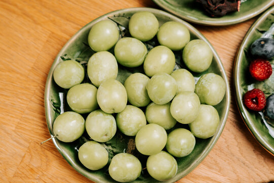 Fresh green plums arranged neatly on a decorative ceramic plate during the bright daylight hours