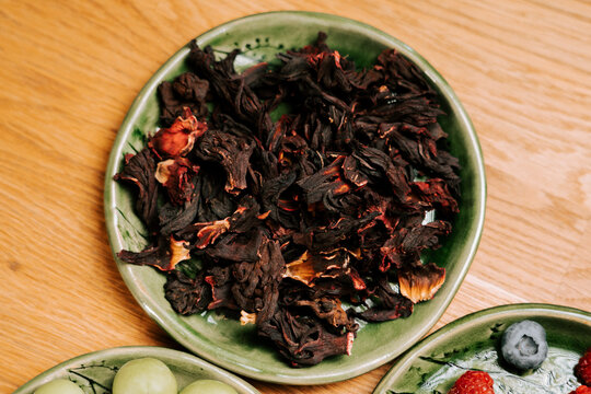 Dried hibiscus petals in a green dish on a wooden table