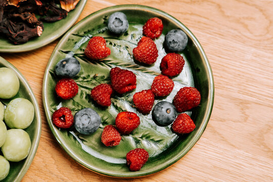 Fresh red raspberries and blue blueberries served on a decorated green ceramic plate for breakfast