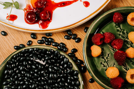 Plates filled with red raspberries and black beans arranged on a wooden table for a morning meal
