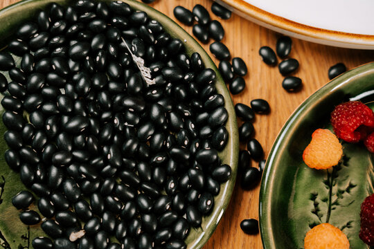 Black beans arranged in green plates next to fresh raspberries on a wooden table during the day