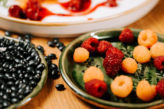 Fresh red and golden raspberries served on a ceramic plate next to a bowl of black beans on a table