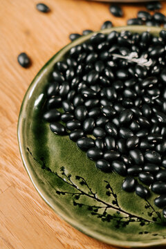 Dried black beans arranged on a decorative green ceramic plate resting on a rustic wooden tabletop