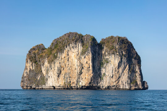 Limestone cliffs on a sea stack in the Andaman Sea near Krabi, Thailand. Blue sky and deep blue ocean.
