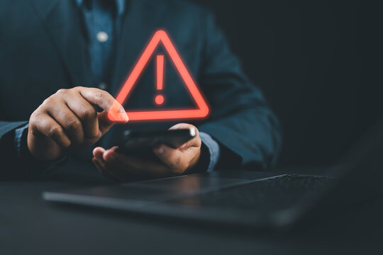 Person using smartphone with warning alert notification symbol on screen for cybersecurity risk, online fraud detection, mobile security protection and digital threat awareness concept.