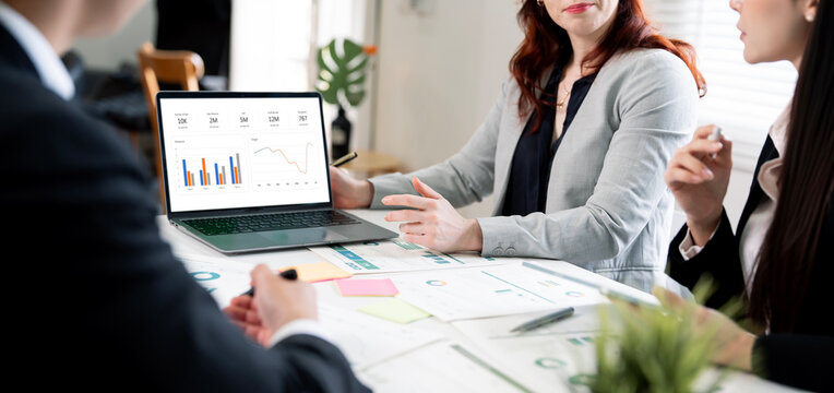Business people discussing financial graph dashboard on laptop during meeting in modern office