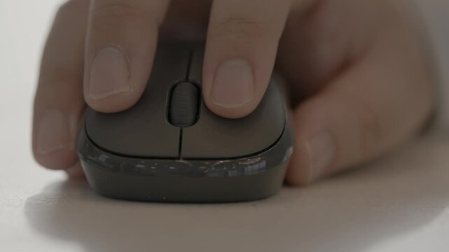 A close-up of a person's hand using a dark ergonomic computer mouse on a desk surface in a casual work setting.
