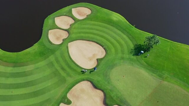 Serious golfers play challenging round on lush green course with distinctive footprint sand traps under overcast sky capturing serene sporting scene; premium golf imagery.