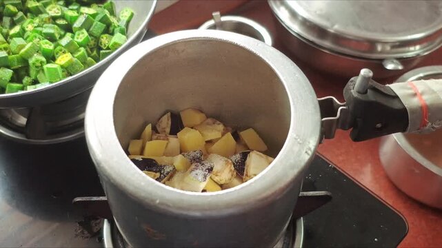 Indian Chef Adding Spices, Chopped Eggplant, Potatoes, and Water into Pressure Cooker for Traditional Curry Cooking
